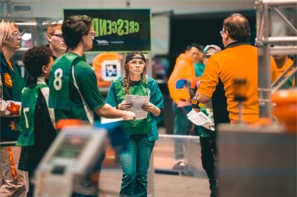 team members in green shirts consult with orange shirt coach at Robotics event